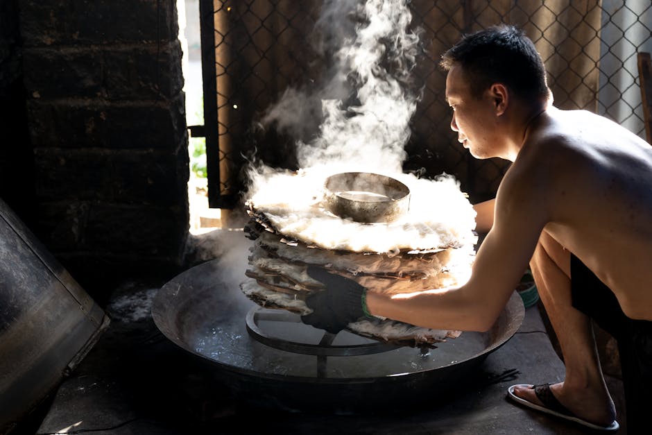 Chef scraping fresh rice noodle rolls (Cheong Fun) from a metal steamer tray