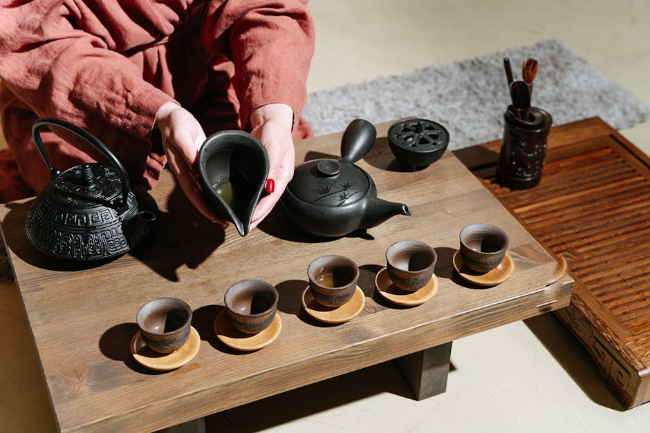 A vintage Yixing clay teapot pouring tea into small cups on a wooden tray