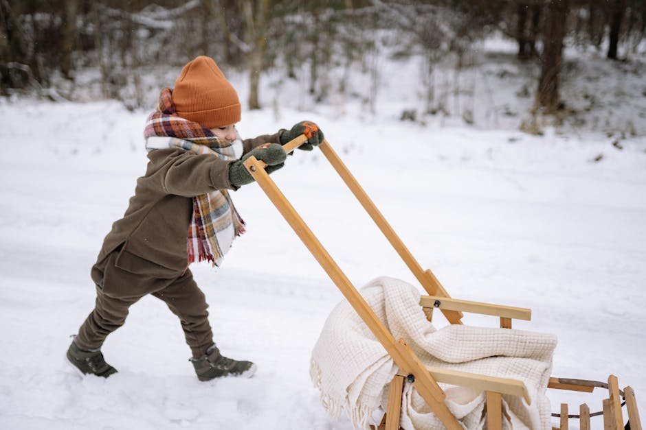 Small child wrapped in thick blankets sitting on a plastic sledge on the ice